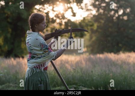 Prag, Tschechische Republik. 02. Juni 2023. Eine Frau in traditioneller Arbeitskleidung schärft die Sense bei Sonnenaufgang. Rund 50 Einheimische kommen zusammen, um Blumenwiesen im Stromovka Park zu mähen, dem größten Park in Prag, der sich in der Nähe des historischen Stadtzentrums befindet. (Foto: Tomas Tkacik/SOPA Images/Sipa USA) Guthaben: SIPA USA/Alamy Live News Stockfoto