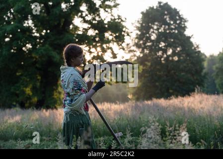 Prag, Tschechische Republik. 02. Juni 2023. Eine Frau in traditioneller Arbeitskleidung schärft die Sense bei Sonnenaufgang. Rund 50 Einheimische kommen zusammen, um Blumenwiesen im Stromovka Park zu mähen, dem größten Park in Prag, der sich in der Nähe des historischen Stadtzentrums befindet. (Foto: Tomas Tkacik/SOPA Images/Sipa USA) Guthaben: SIPA USA/Alamy Live News Stockfoto