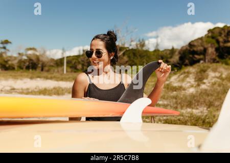 Eine junge Frau steht selbstbewusst neben ihrem Surfbrett an einem sonnenüberfluteten Strand Stockfoto