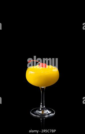 Ein Glas Ananas-Mango-Daiquiri-Cocktail mit roter Kirsche isoliert auf schwarzem Hintergrund. Frischer alkoholischer Cocktail. Stockfoto