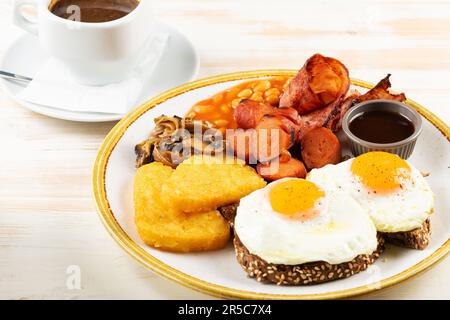 Spiegeleier mit Würstchen, Nuggets, Pilzen und einer Tasse Kaffee. Βreakfast-Konzept. Stockfoto
