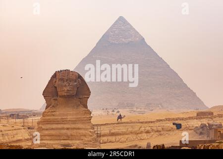 Blick auf die Sphinx auf dem Gizeh-Plateau mit der Großen Pyramide von Gizeh oder der Khufu-Pyramide im Hintergrund bei trüben Tagen, Kairo, Ägypten Stockfoto