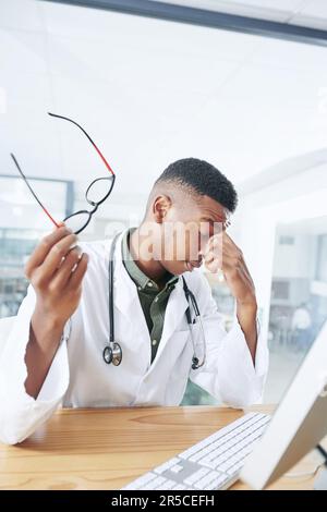 Oh nein, wie ich vermutet habe. Ein gutaussehender junger Arzt, der allein in seiner Praxis in der Klinik sitzt und sich gestresst mit seinem Computer fühlt. Stockfoto