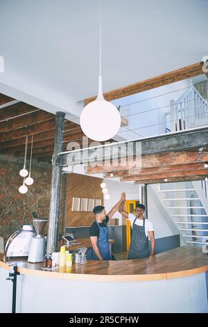 Motivation macht den Kaffee so gut wie er ist. Zwei selbstbewusste junge Männer geben sich gegenseitig ein High Five, während sie in einem Café arbeiten. Stockfoto