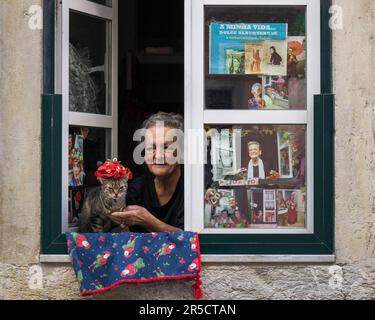 Lissabon, Portugal. 10.05.2023. Eine berühmte ältere Einwohnerin von Lissabon sitzt am Fenster mit ihrer Katze im Hut. Portugal Stockfoto