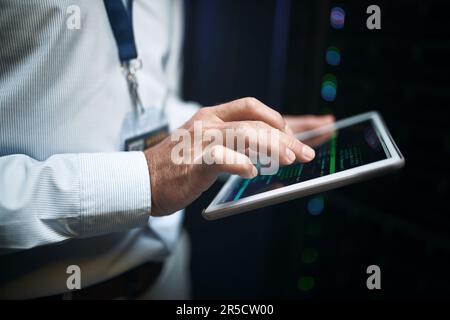 Verbesserung der Kapazität der Systeme. Nahaufnahme eines unbekannten Mannes, der ein digitales Tablet benutzt, während er in einem Serverraum arbeitet. Stockfoto