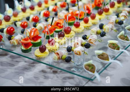 Auf einem Glastisch werden verschiedene Snacks und Häppchen serviert. Das Essen war sehr schön gestaltet und ausgelegt. Catering für die Feiertage. Heller Hintergrund. Stockfoto