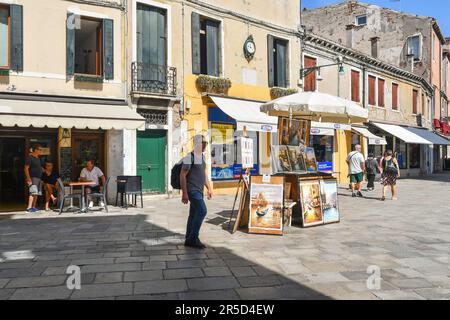 Souvenirgemälde unter einem Schirm in Rio Terà San Leonardo mit Leuten im Straßencafè im Sommer, Venedig, Veneto, Italien Stockfoto