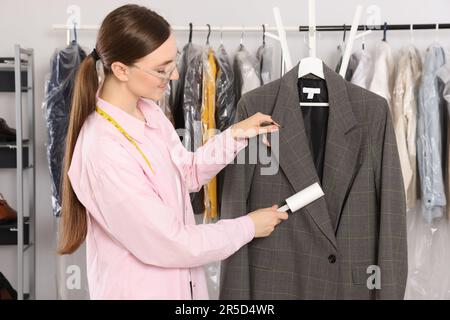 Junge Frau, die bei der Trockenreinigung einen Kleber-Fusselroller benutzt Stockfoto