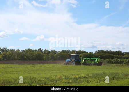 Moderne Traktor-Erntemaschine auf dem landwirtschaftlichen Feld an sonnigen Tagen Stockfoto