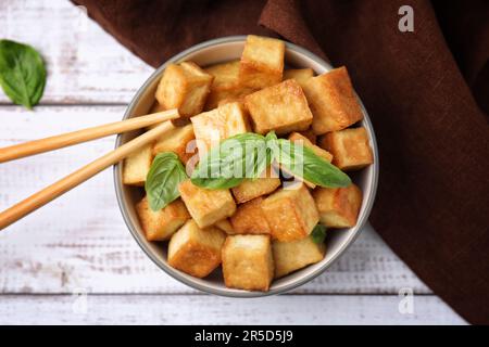 Schüssel mit köstlichem gebratenem Tofu, Basilikum auf weißem Holztisch, flach liegend Stockfoto