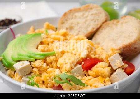 Schüssel mit köstlichem Rührei, Tofu und Scheiben Baguette, Nahaufnahme Stockfoto