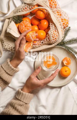 Frau mit köstlichen reifen Tangerinen und einem Glas Sekt auf weißem Bettlaken, Draufsicht Stockfoto