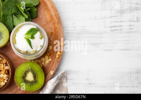 Köstliches Dessert mit Kiwi, Joghurt und Müsli auf weißem Holztisch, flach liegend. Platz für Text Stockfoto