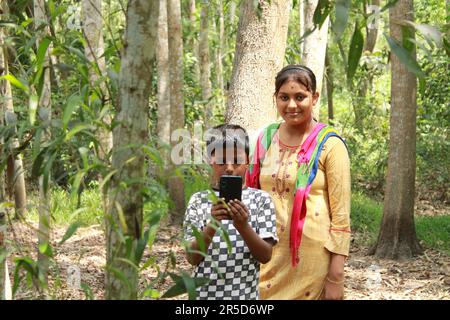 Indische Landjunge und Mädchen, die im Freien ein Handy benutzen. Stockfoto