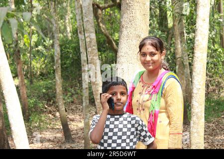 Indische Landjunge und Mädchen, die im Freien ein Handy benutzen. Stockfoto