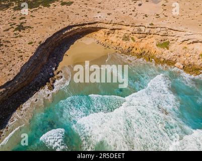 Aus der Vogelperspektive sehen Sie Wellen, die in eine kleine Bucht an einer zerklüfteten Küste der Venus Bay auf der Eyre-Halbinsel in Südaustralien einbrechen. Stockfoto