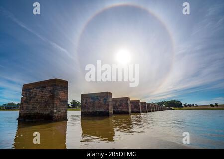 Blick aus dem niedrigen Winkel auf einen Solar Halo über Ruinen von Viaduktsäulen in einem See am Cairn Curran Reservoir im Zentrum von Victoria, Australien Stockfoto