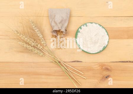 Weizenzapfen mit Mehl und Körnern in einem braunen Sack auf Holzhintergrund Stockfoto