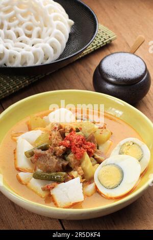 Nahaufnahme Lontong Sayur Padang mit gekochten Eiern und Crackern, indonesische traditionelle Speisen aus gepacktem Reis mit vegetarischem Eintopf. Stockfoto