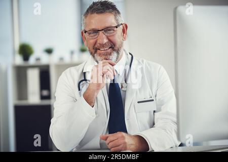 Ich werde mein Bestes tun, damit es dir gut geht. Porträt eines reifen Arztes, der an einem Schreibtisch in seiner Praxis arbeitet. Stockfoto