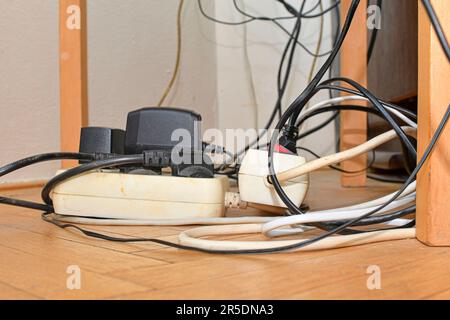 Verwickelte Kabel auf dem Parkettboden. Überlastete Schalttafeln auf dem Holzboden. Elektrische Kabel bei Störungen. Stockfoto