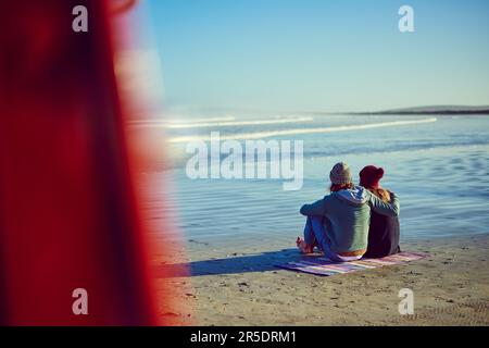 Liebe ist eine schöne Sache. Rückblick auf ein junges Paar, das am Strand sitzt. Stockfoto