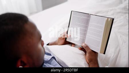Glücklicher Junger Afrikanischer Mann, Der Sein Buch Über Das Bett Liest Stockfoto