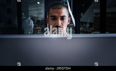 Direkte berufliche Hingabe. Ein junger Geschäftsmann, der nachts einen Computer in einem modernen Büro benutzt. Stockfoto