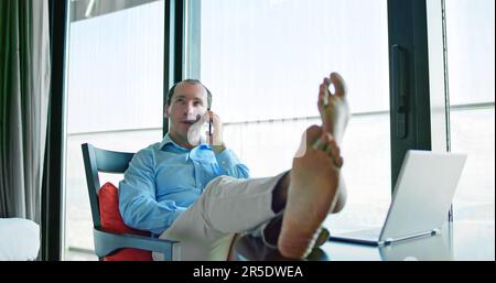 Entspannter Junger Geschäftsmann, Der Mit Den Füßen Am Schreibtisch Sitzt Stockfoto