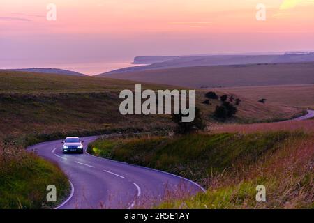 Ein Auto, das auf einer kurvenreichen Straße in East Sussex mit dem Leuchtturm Belle Tout und dem Ärmelkanal in der Ferne fährt. Stockfoto