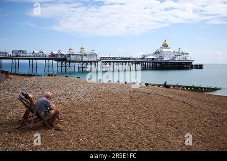 Eastbourne, East Sussex | UK - 4 August 2021: Ein mittelalterlicher Sitzplatz in Liegestühlen am Strand mit dem berühmten viktorianischen Pier im Hintergrund. Stockfoto