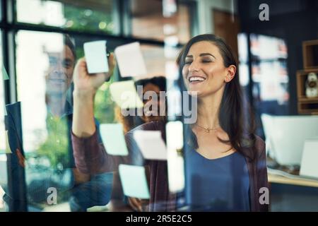 Planung ist erst der Anfang einer weiteren Erfolgsgeschichte. Eine Gruppe von Geschäftsleuten, die mit Notizen an einer Glaswand in einem Büro Brainstorming durchführen. Stockfoto