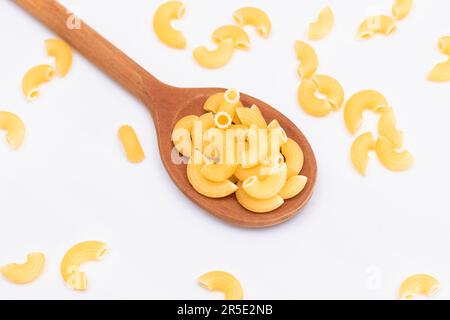 Ungekochte Chifferi Rigati Pasta in Holzlöffel auf weißem Hintergrund. Fett und ungesunde Lebensmittel. Verstreute Klassische Trockene Makkaroni. Italienische Kultur und Küche. Rohe Pasta Stockfoto