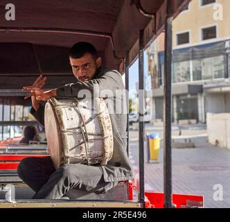 Sousse, Tunesien, 22. Januar 2023: Junger tunesischer Musiker, der in einem offenen Personenzug eine große Handtrommel spielt, um die Passagiere zu unterhalten Stockfoto