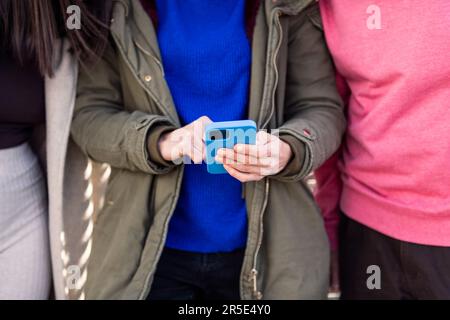 Hände einer Frau, die mit Freunden ein Smartphone benutzt Stockfoto