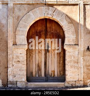 Sousse, Tunesien, 22. Januar 2023: Verwitterte massive antike Holztür in einem Steinbogen in der alten Mauer der Altstadt, Medina, von Sousse Stockfoto