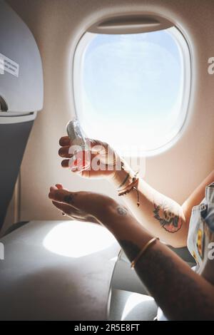 Schützen Sie sich und andere. Eine Frau, die ihre Hände im Flugzeug desinfiziert. Stockfoto