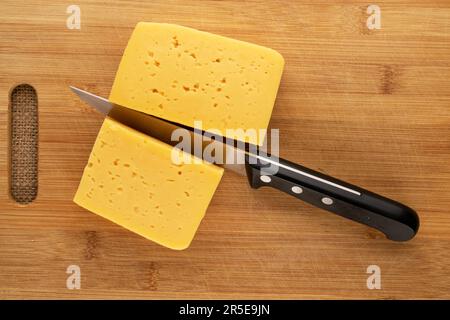 Schneiden Sie Käse mit einem Messer auf einem hölzernen Küchenbrett, Makro, Draufsicht. Stockfoto