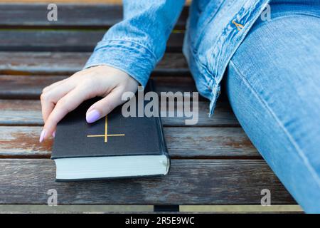 Eine Frau, die ihre Hand an der bibel hielt, die auf der Bank lag. Eine Frau mit der papierbibel Stockfoto