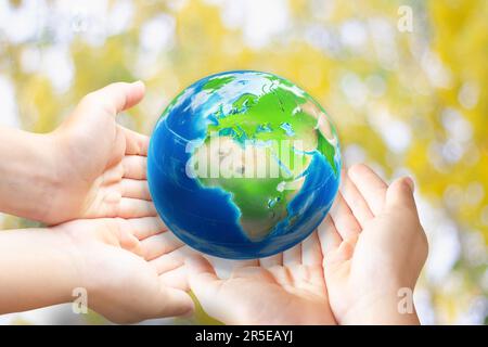 Erde in Form Wassertropfen von der Spitze der Kinderhand auf grünem Hintergrund für das internationale Wassertagkonzept oder den Weltumwelttag Stockfoto