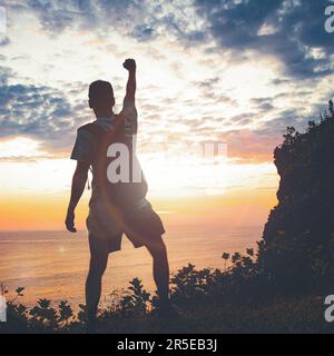 Ein Mann, der die Fäuste am Sonnenuntergang erhebt. Sieg und Triumph der Menschen. Stockfoto