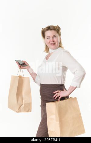 Reife Frau, die Einweg-Papiertüten mit Einkäufen nach dem Einkaufen hält, mit Handy. Kaukasierin, ethnische Frau Stockfoto