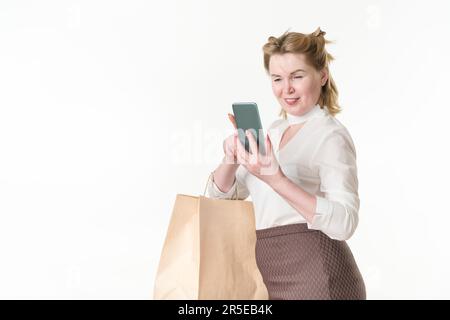 Fröhliche Frau beim Einkaufen, mit dem Smartphone auf den Bildschirm schauen, Online-Nachrichten lesen und Angebote mit Sonderangeboten und Rabatten durchstöbern Stockfoto