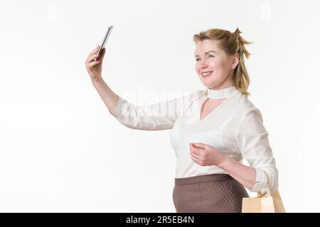 Lächelnde, elegante, 49 Jahre alte Frau mit Smartphone und Einkaufstasche. Konzepte für Verkäufe und Rabatte. Kaukasierinnen Stockfoto