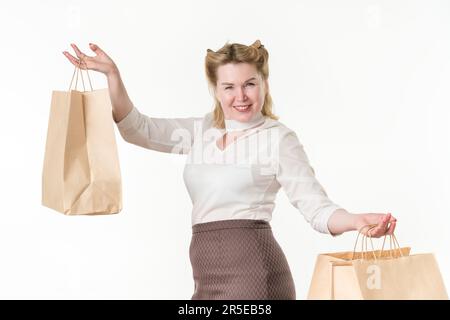 Fröhliche blonde Frau, die lächelt und in die Kamera schaut. Erwachsene im mittleren Alter, weibliche Shopaholic, die Einwegbeutel aus Papier auf weiß hält Stockfoto