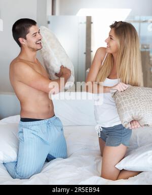 Ich habe Spaß. Süßes junges Paar, das eine Kissenschlacht auf dem Bett hat. Stockfoto