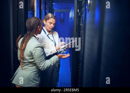 Sie verfügen über das technische Know-how, um Fehler zu beheben. Zwei Techniker, die ein digitales Tablet verwenden, während sie in einem Serverraum arbeiten. Stockfoto