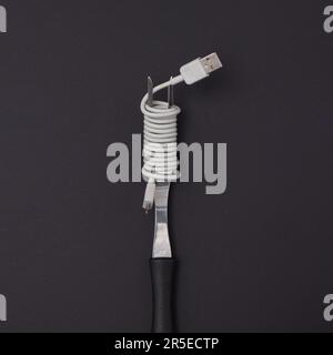 Eine Gabel mit einem USB-Kabel, umwickelt wie Spaghetti auf schwarzem Hintergrund. Minimaler Lebensstil. Stockfoto