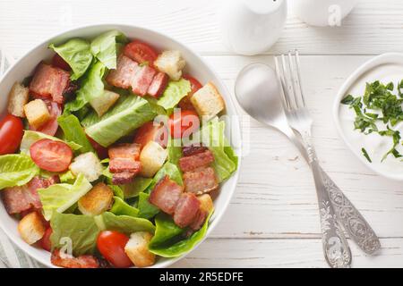 BLT-Salat mit Römersalat, knusprigem Speck, Tomaten, knusprigen Croutons und einem cremigen Knoblauchdressing auf dem Teller auf dem Tisch. Ge Stockfoto